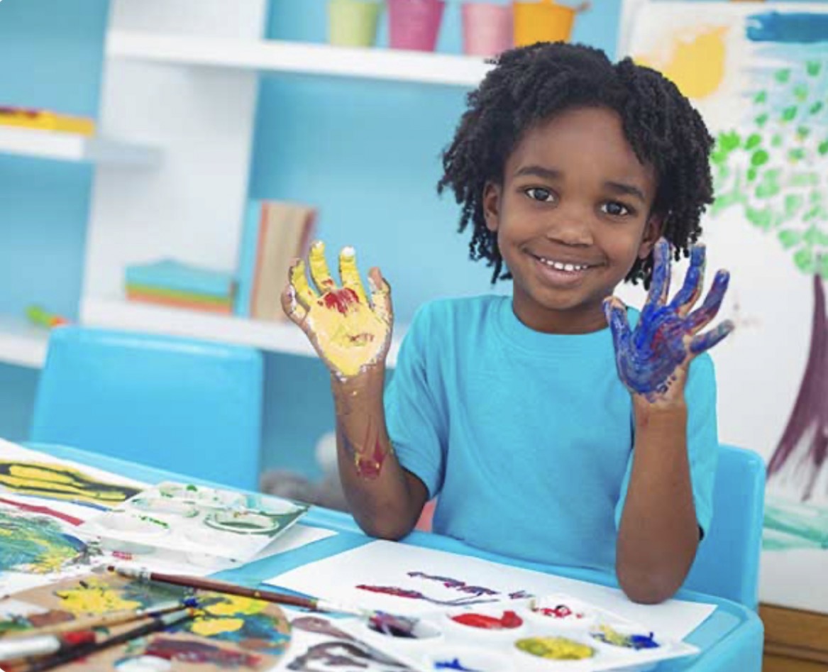 A smiling child showing colorful painted hands during an art activity